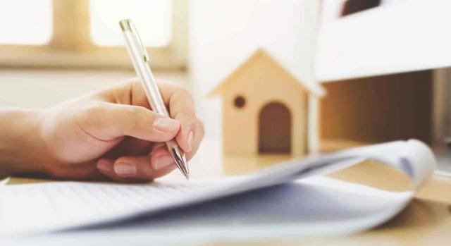 Crédito Crédito. Primer plano de una mano firmado un contrato y una casa de madera al lado