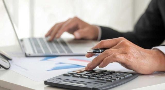 Nuevos cambios en el Informe de Auditoría: El ICAC actualiza las NIA-ES. Imagen de un hombre trabajando con su portátil y calculadora