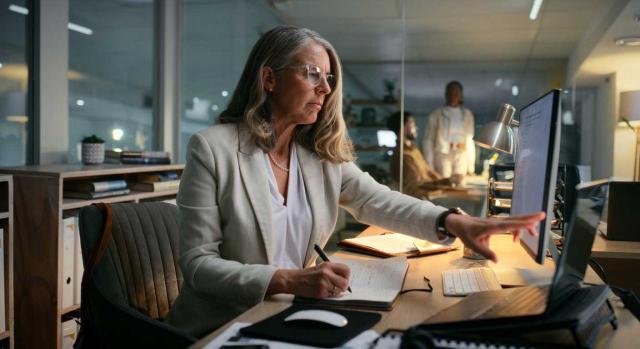 Información en la memoria sobre activos y pasivos derivados de contratos según el PGC y la RICAC Sobre la información que hay que incluir en la memoria sobre activos y pasivos derivados de contratos por ventas de bienes y prestación de servicios. Imagen de una mujer trabajando en su oficina ya de noche