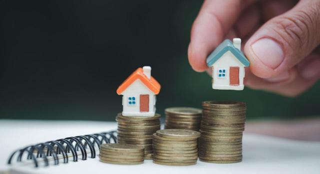 Caso practico sobre la reclasificación de las inversiones inmobiliarias a existencias Caso practico sobre la reclasificación de las inversiones inmobiliarias a existencias. Imagen de persona sosteniendo una casa en miniatura sobre un montón de monedas